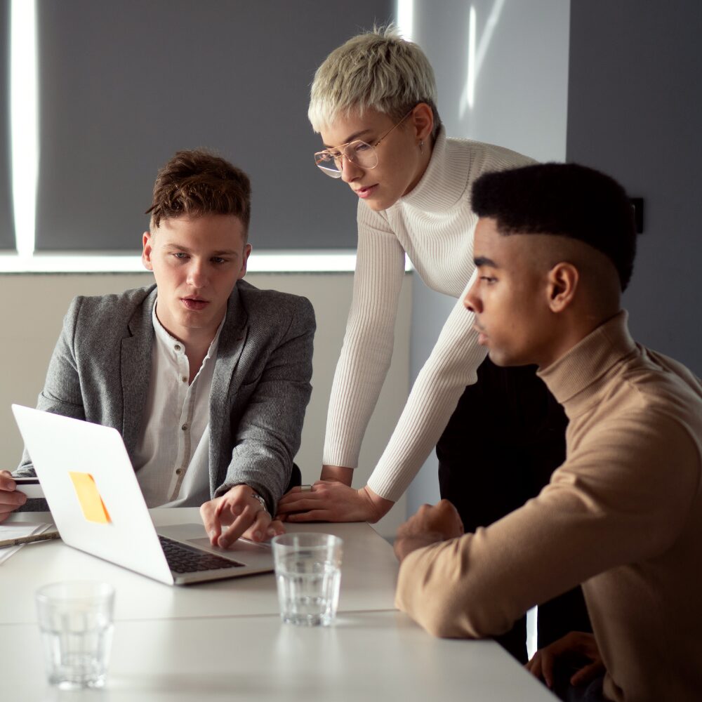 A group of three people in an office, gathered around a laptop looking at their work